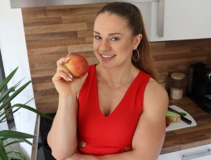 Coach Johanna is smiling with an apple in her hand at her kitchen.