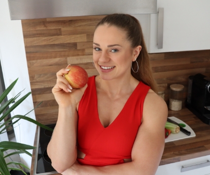 Coach Johanna is smiling with an apple in her hand at her kitchen.